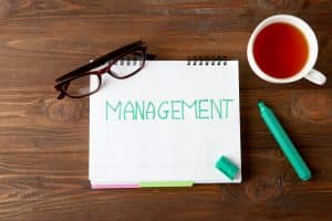 Notebook withניהול משימות או ניהול פרויקטים - written word MANAGEMENT, eyeglasses and cup of tea on table